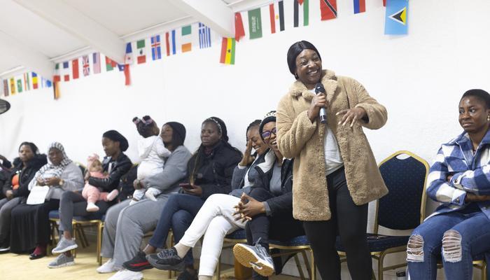 A woman standing up with a microphone laughs as she shares with the group