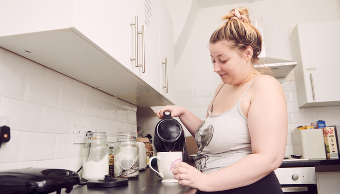 A woman is pouring hot water from a kettle. You can see various kitchen items around them