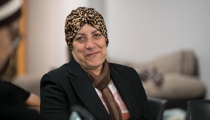 A lady wearing a hair turban, is looking towards the camera, smiling