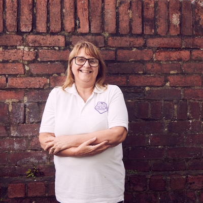 Caroline Johnson, Director of Amazing Grace Space in Newport, Wakes is standing with har arms crosses in front of a brick wall. She is smiling and looking towards to camera.